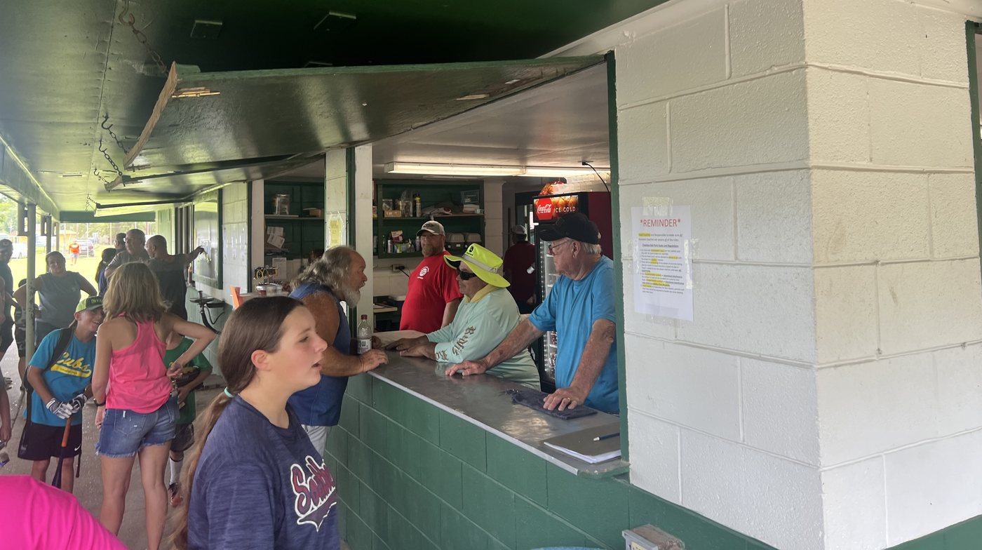 A line of people at the concession stand counter at Schneider Park, with three adults serving from inside the stand
