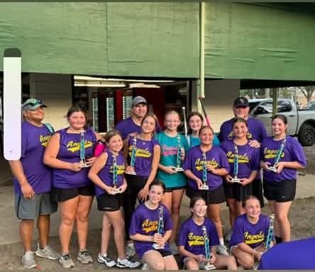A team in purple Angels shirts holding trophies in front of the concession stand