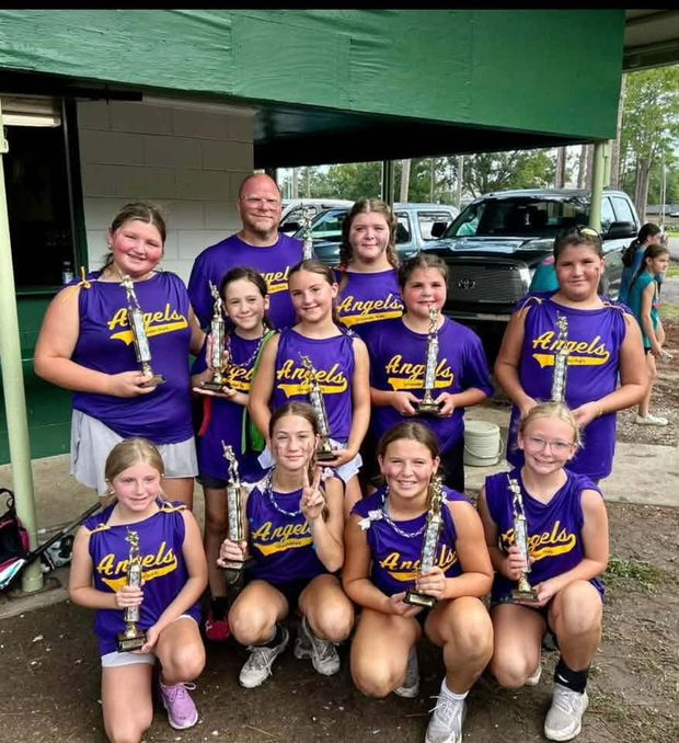 A team in purple Angels shirts holding trophies in front of the dugout