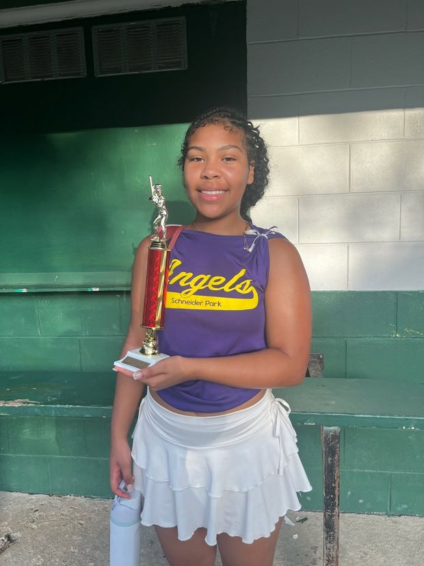A girl in a purple Angels top holding a trophy inside the dugout