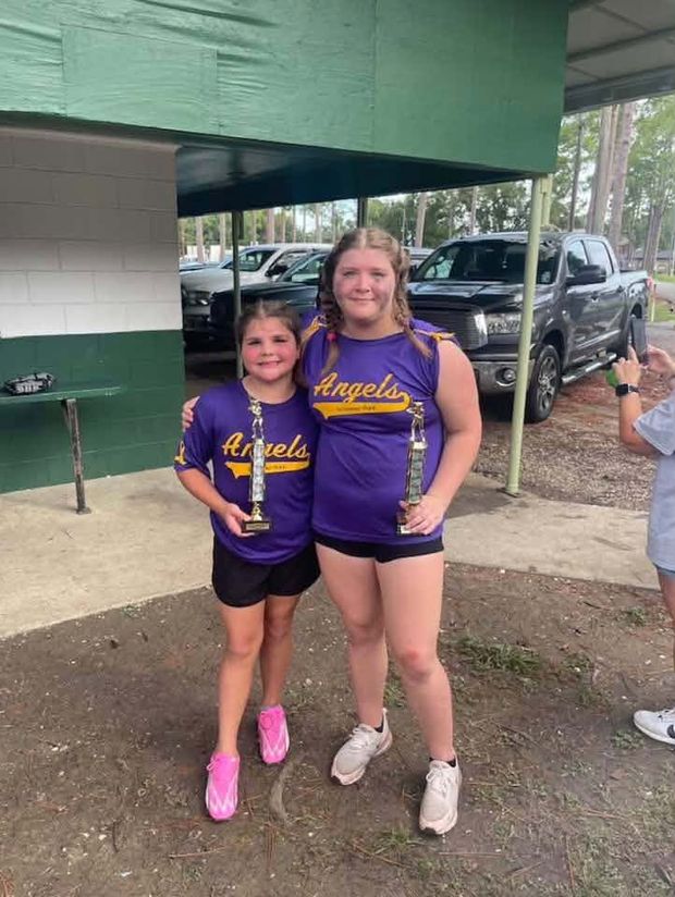 An older girl and a younger girl in purple Angels shirts, one holding a trophy