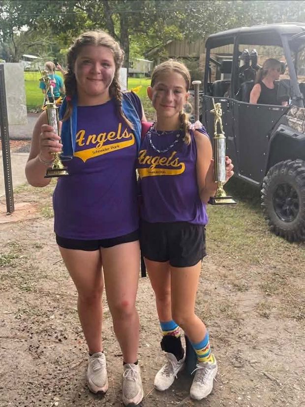 Two girls in purple Angels shirts each holding a tall trophy