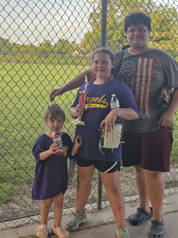Three children standing together, one holding an Angels trophy