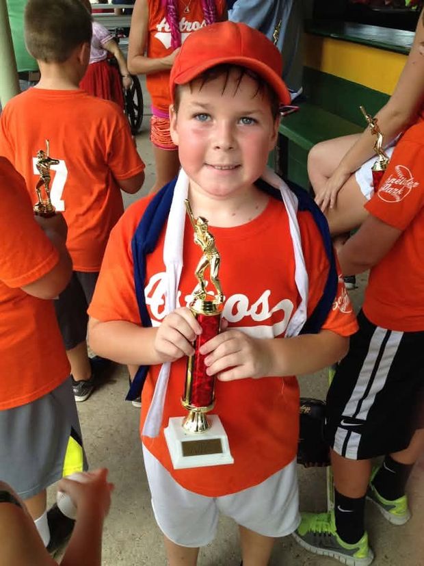 A boy in an orange Astros shirt and red cap holding a red trophy among his teammates