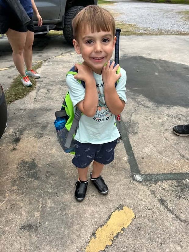 A small boy with a backpack raising his hands in the parking lot