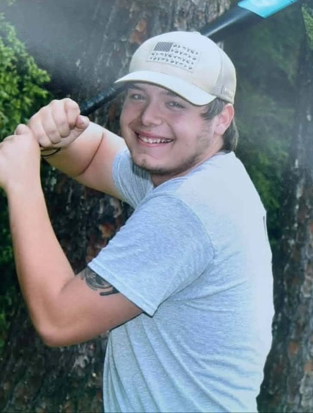 A teenager in a cap holding a bat in a batting pose by a tree