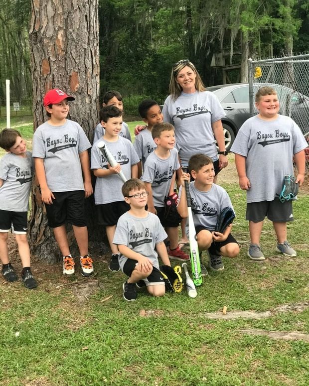 A boys team in grey Bayou Boys shirts posed around a tree