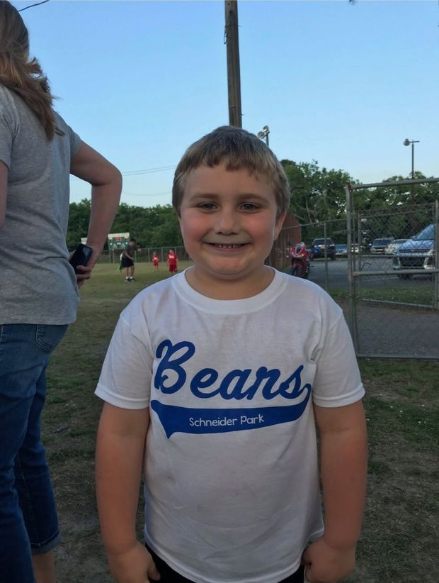 A boy in a white Beans team shirt smiling at the park