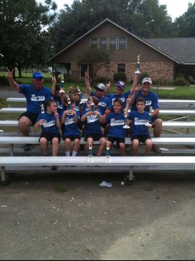 A team of boys in blue Bears shirts sitting on bleachers with their coaches, holding trophies