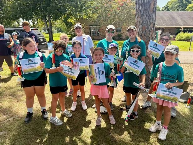 Girls in teal Blackcats shirts holding trophies and paper certificates outdoors