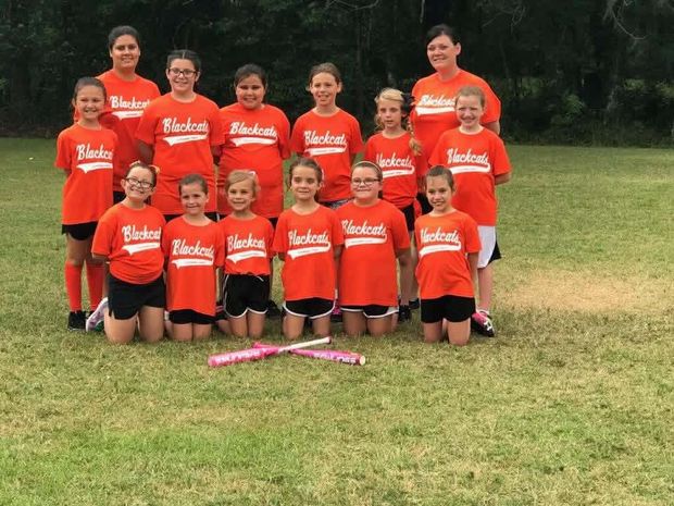 A girls team in orange Blackcats shirts posed in rows on the grass
