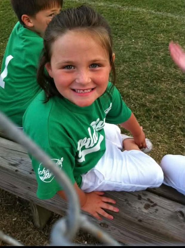 A little girl in a green shirt sitting on the bleachers