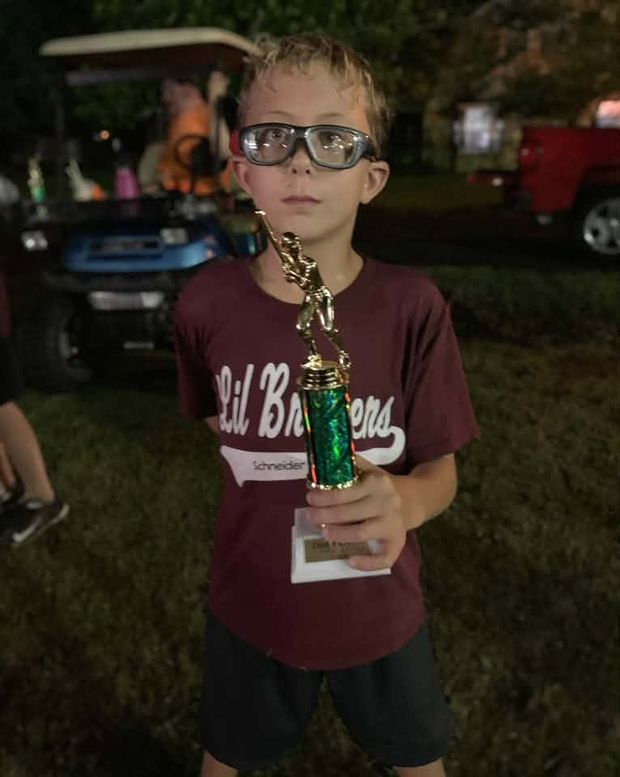 A boy in a maroon Lil Bruisers shirt holding a green trophy at night