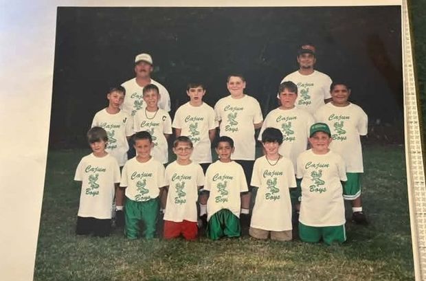 A printed team photograph of young players in cream Cajun Boys shirts carrying a green alligator emblem, arranged in three rows