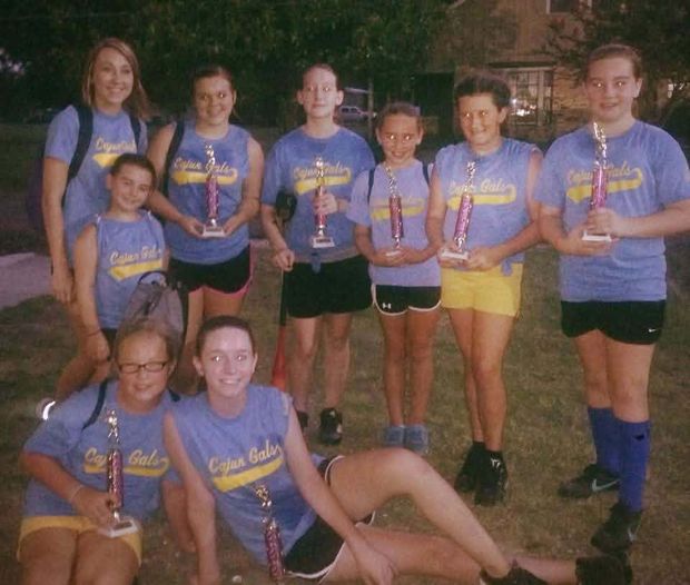 A team in Cajun Gals shirts holding trophies at night