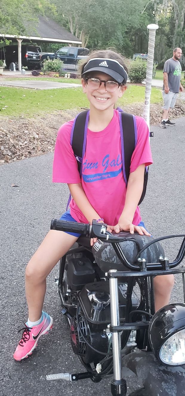 A girl in a pink Cajun Girls shirt sitting on a small motorbike