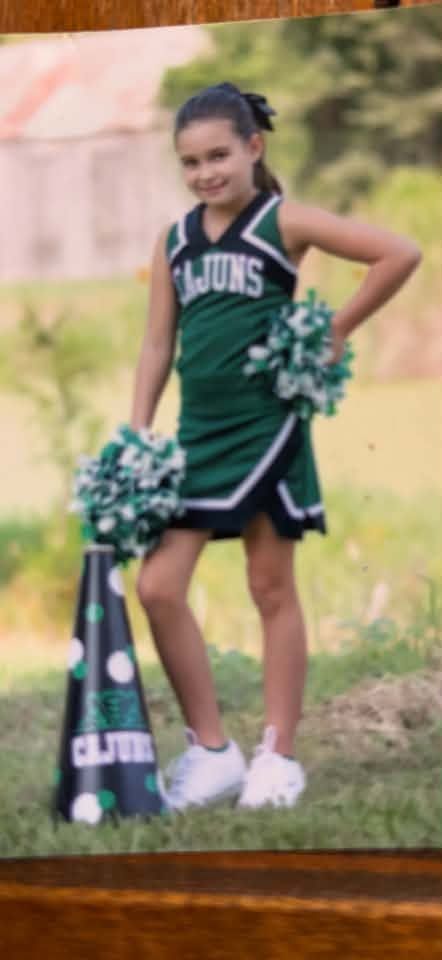 A printed photograph of a cheerleader in a green Cajuns uniform posing with pompoms