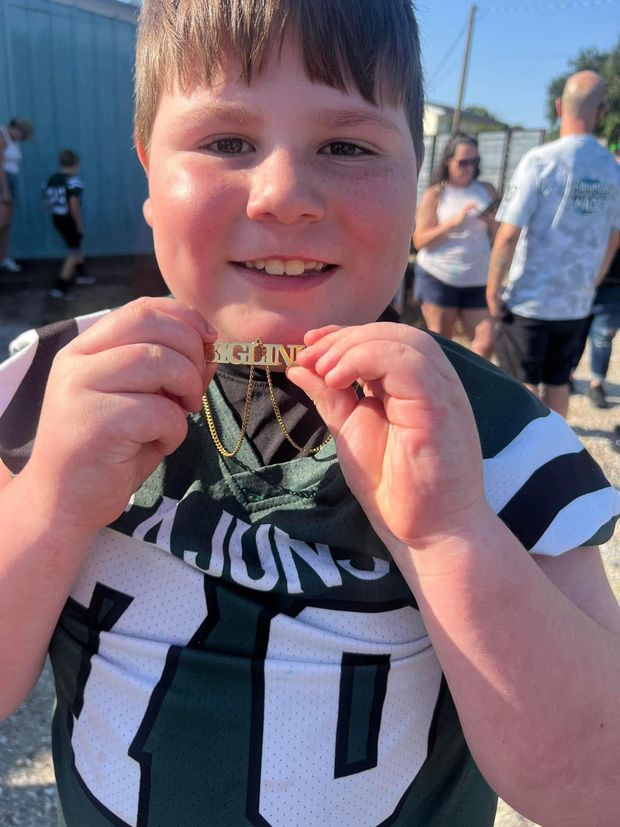 A young football player in a Cajuns jersey holding up a gold nameplate chain