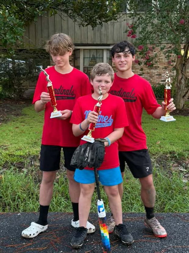 Three boys in red Cardinals shirts holding trophies