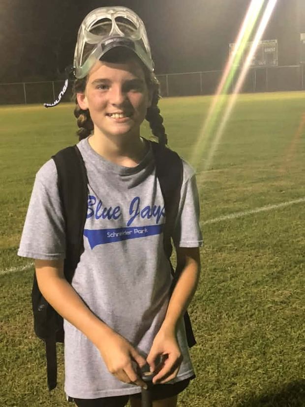 A girl in a grey Blue Jays shirt with a catchers mask pushed up on her head at night