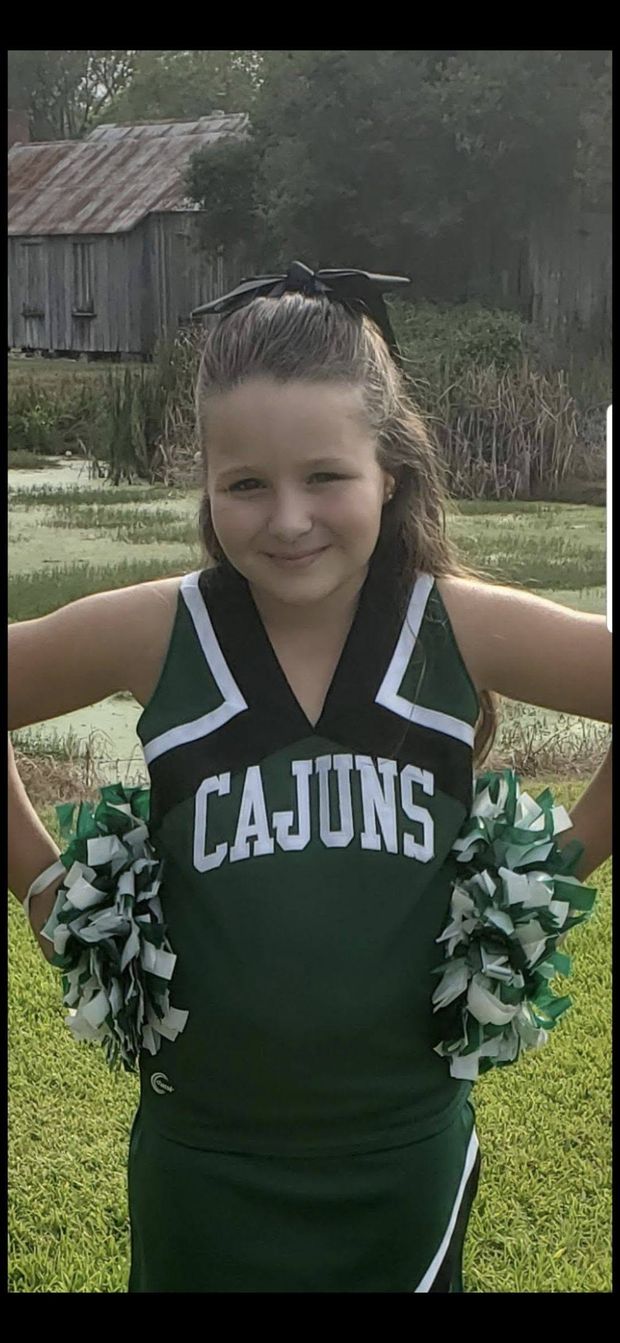 A girl in a green Cajuns cheerleading uniform posing outdoors
