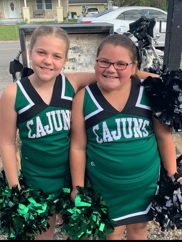 Two cheerleaders in green Cajuns uniforms standing together with pompoms