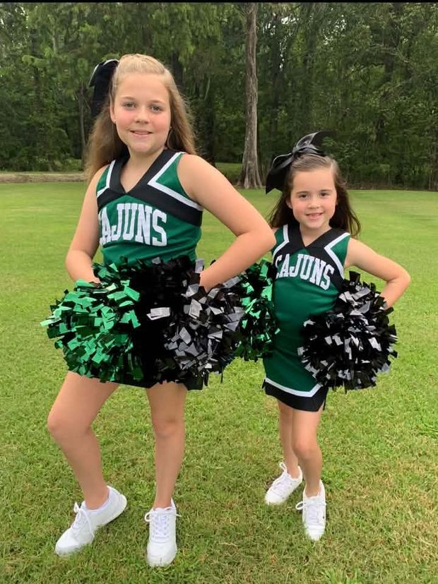 Two cheerleaders in green and white Cajuns uniforms posing on the grass with pompoms