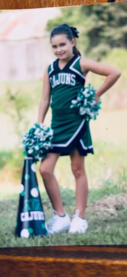 A printed photograph of a cheerleader in a green Cajuns uniform with a megaphone