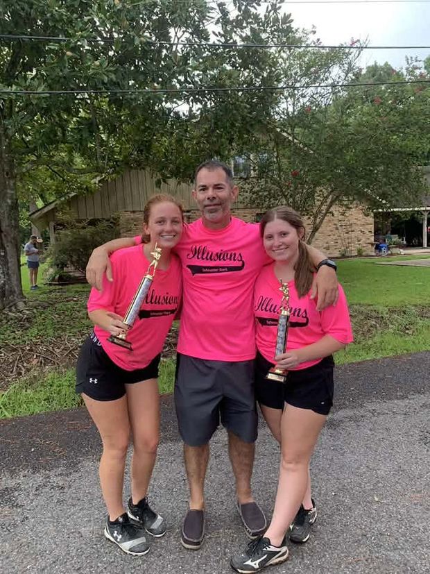 A man standing between two players in pink team shirts, each of them holding a trophy