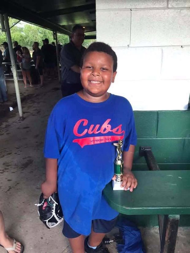 A boy in a blue Cubs shirt holding a green trophy and a glove in the dugout