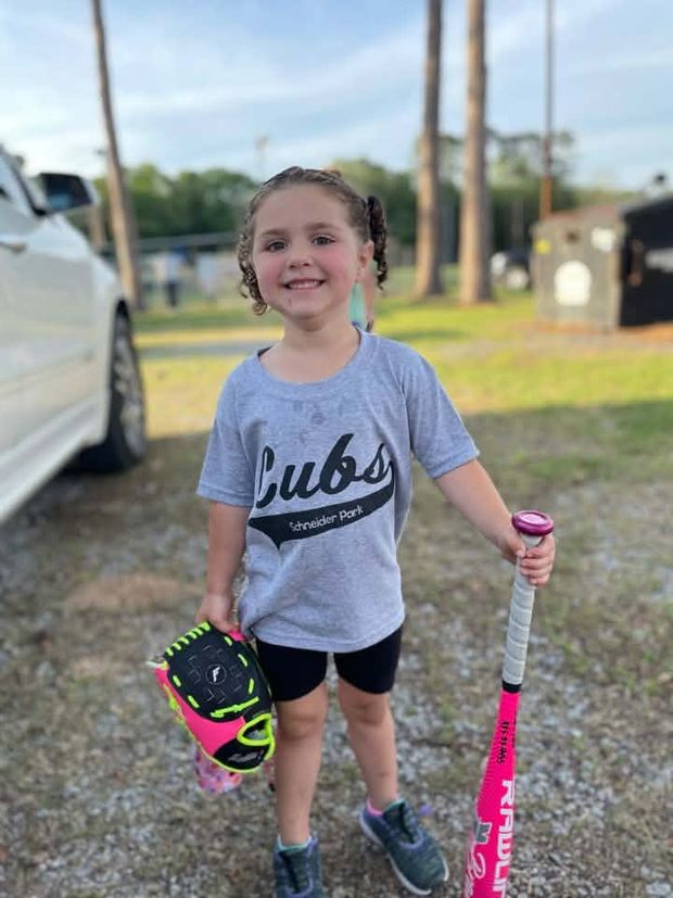 A girl in a grey Cubs shirt holding a pink bat and glove