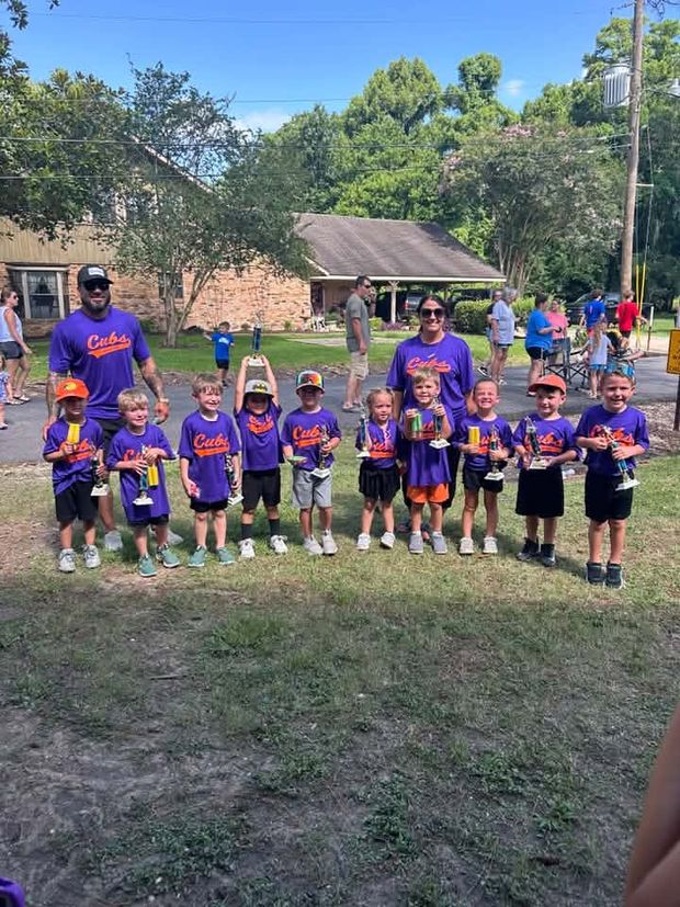Small children in purple Cubs shirts holding trophies with their coaches
