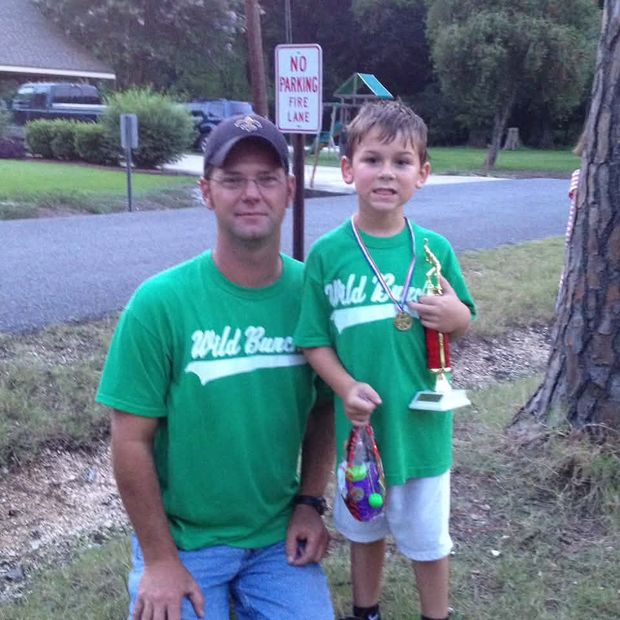 A man crouched beside a small boy, both in green Wild Bunch shirts, the boy holding a trophy and wearing a medal
