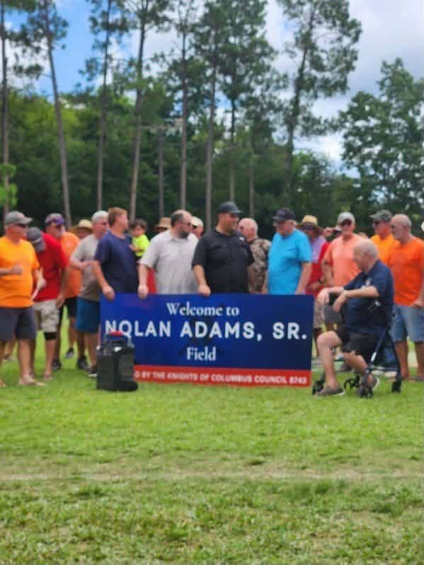 People holding the Nolan Adams Sr Field banner on the field