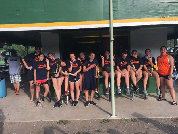 A softball team in navy shirts sitting and standing along the bench inside the covered dugout