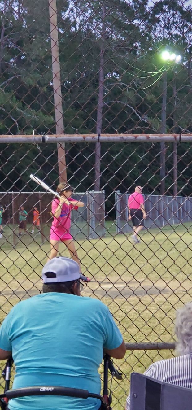 A batter at the plate at dusk seen past spectators at the fence