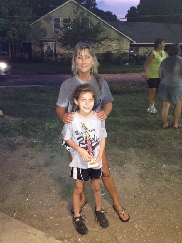 A woman standing behind a girl in a team shirt who is holding a trophy at dusk