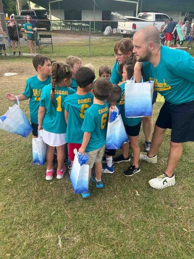 A coach in teal handing gift bags to small children in team shirts