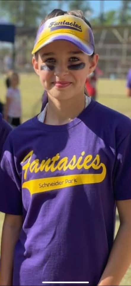 A girl in a purple Fantasies shirt and visor with eye black on her cheeks