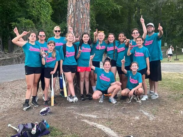 A team in teal shirts posed on the field pointing upward