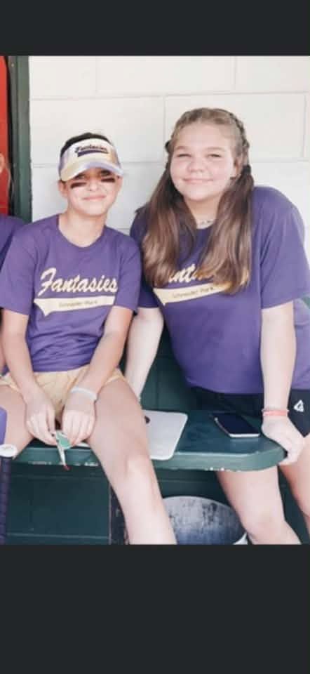 Two children in purple Fantasies shirts sitting together in the dugout