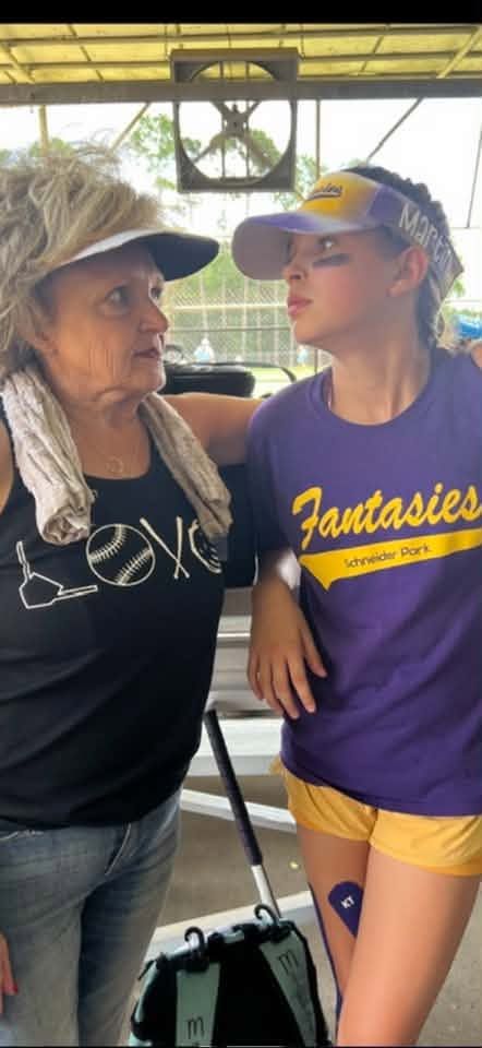 An older woman standing with a girl in a purple Fantasies shirt at the bleachers