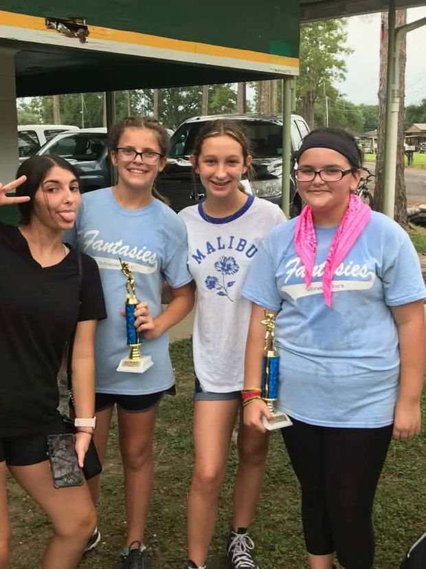 Four girls in light blue team shirts standing together, two of them holding trophies