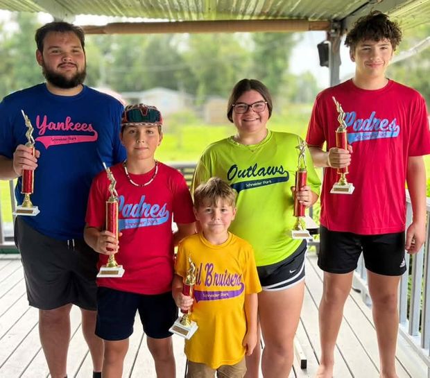 Five children of different ages in different team shirts holding trophies on a porch