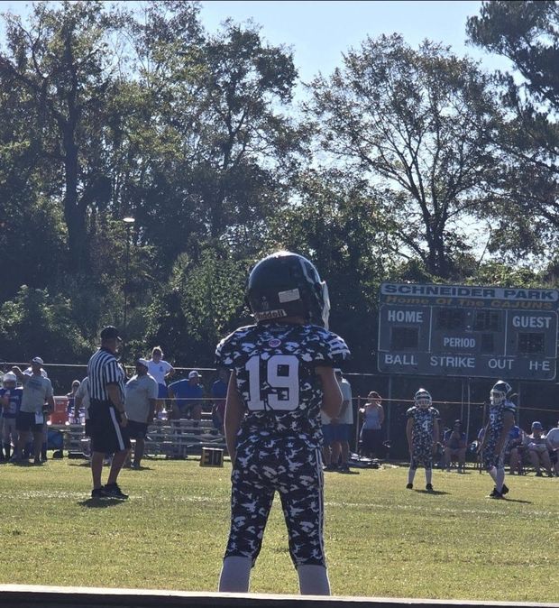 A small football player in uniform standing near the bench at a game