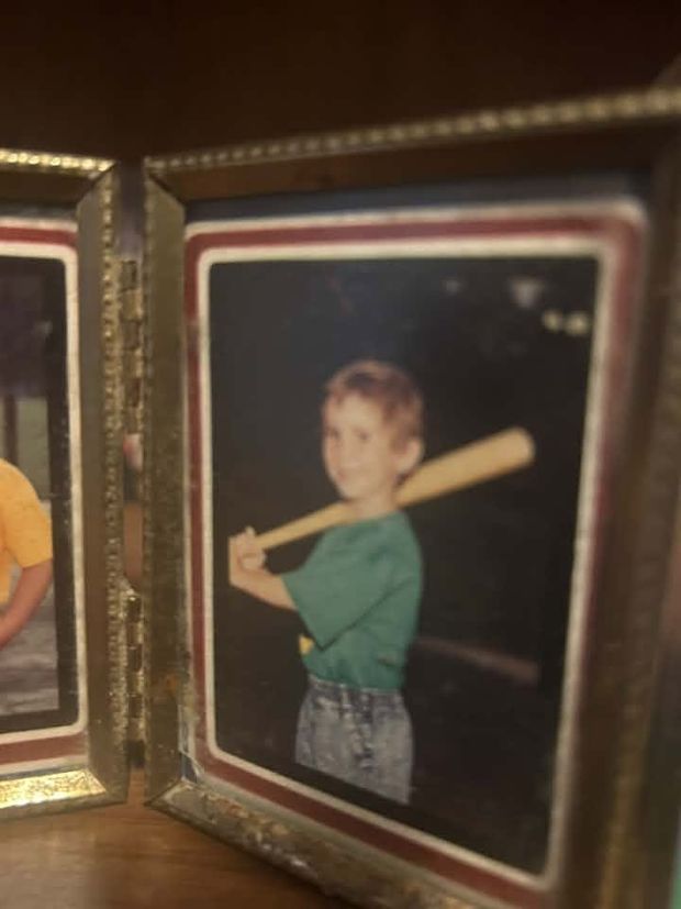 A hinged gold frame holding an old print of a boy in a green shirt with a bat over his shoulder