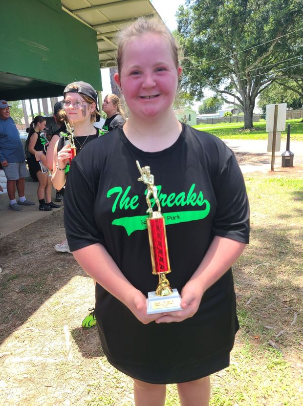 A girl in a black The Freaks shirt holding a red trophy