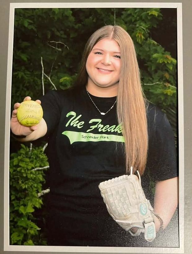 A matted print of a girl in a black Freaks shirt holding up a softball with a glove on her arm