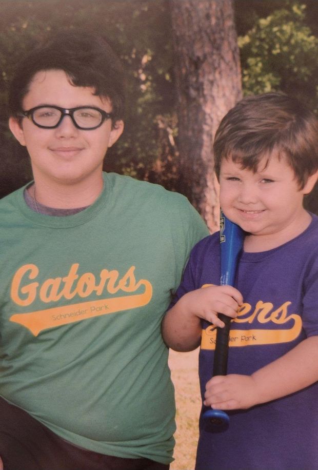 Two boys in Gators and Tigers shirts standing together, one holding a bat
