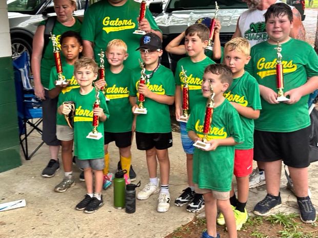 Children in green Gators shirts holding trophies beside a parked car